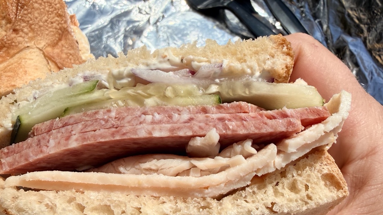 A half of the Salami Mommy in hand — salami and turkey under cucumber, red onion and cream cheese
