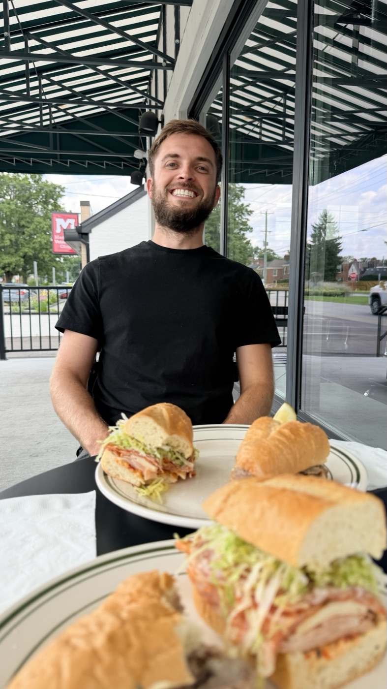 Shay Scarberry at a table at Danny Boy, behind three plated subs