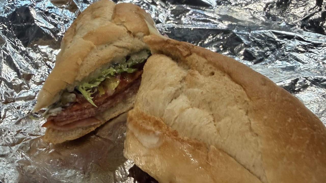 The Hot Italian, cut in two on crumpled foil, salami, ham and pepperoni under banana peppers and greens on a soft toasted baguette