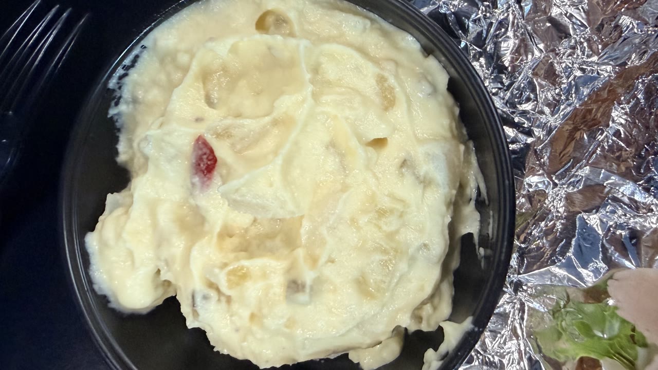A black bowl of very creamy potato salad from above, with a fleck of pimento and sweet relish