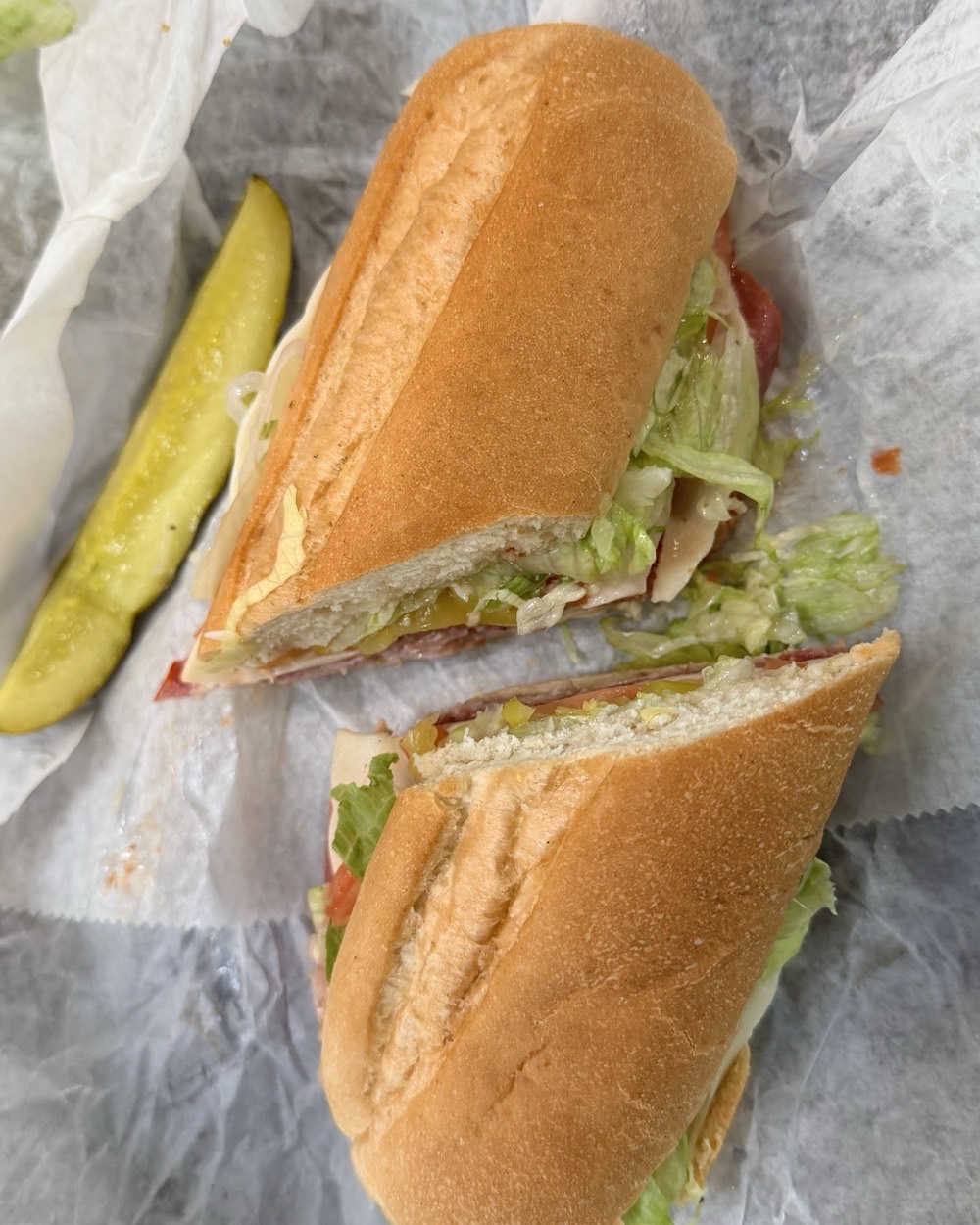 The Little Italy cut into two halves on wax paper with a pickle spear alongside