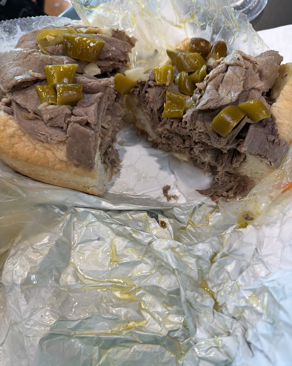 The Italian Beef from Knuckles, cut in two on foil-lined paper, a mountain of thin-sliced beef piled on a soft roll under pickled hot peppers, jus soaking into the wrapper