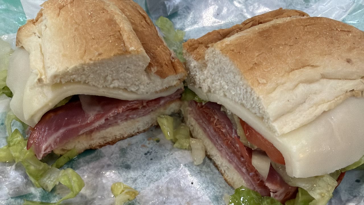 The Italian, cut in half on green-and-white checked paper — prosciutto, salami and pepperoni under a fold of provolone, with tomato and a lot of loose lettuce