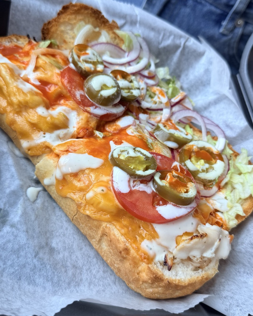 The Angry Bird open-faced on wax paper — buffalo chicken under melted cheese with ranch, jalapeno, tomato and red onion