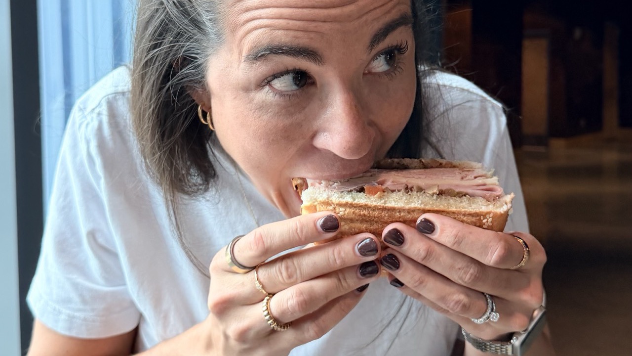 Sarah mid-bite into a half of the Turkey Muffuletta at a window table